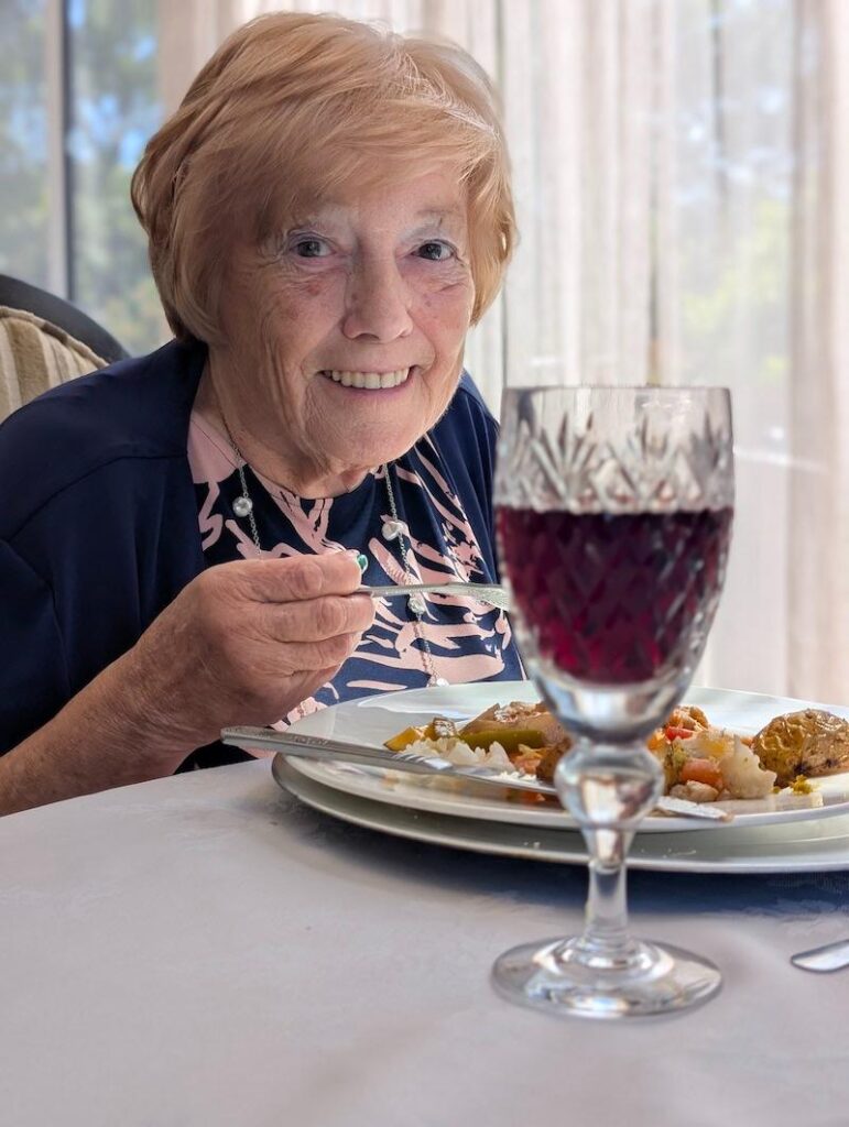 resident smiling with their dinner and wine