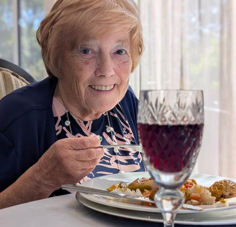 resident smiling with their dinner and wine