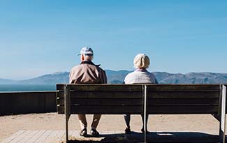 An elderly couple sit on a bench looking out over a cliff