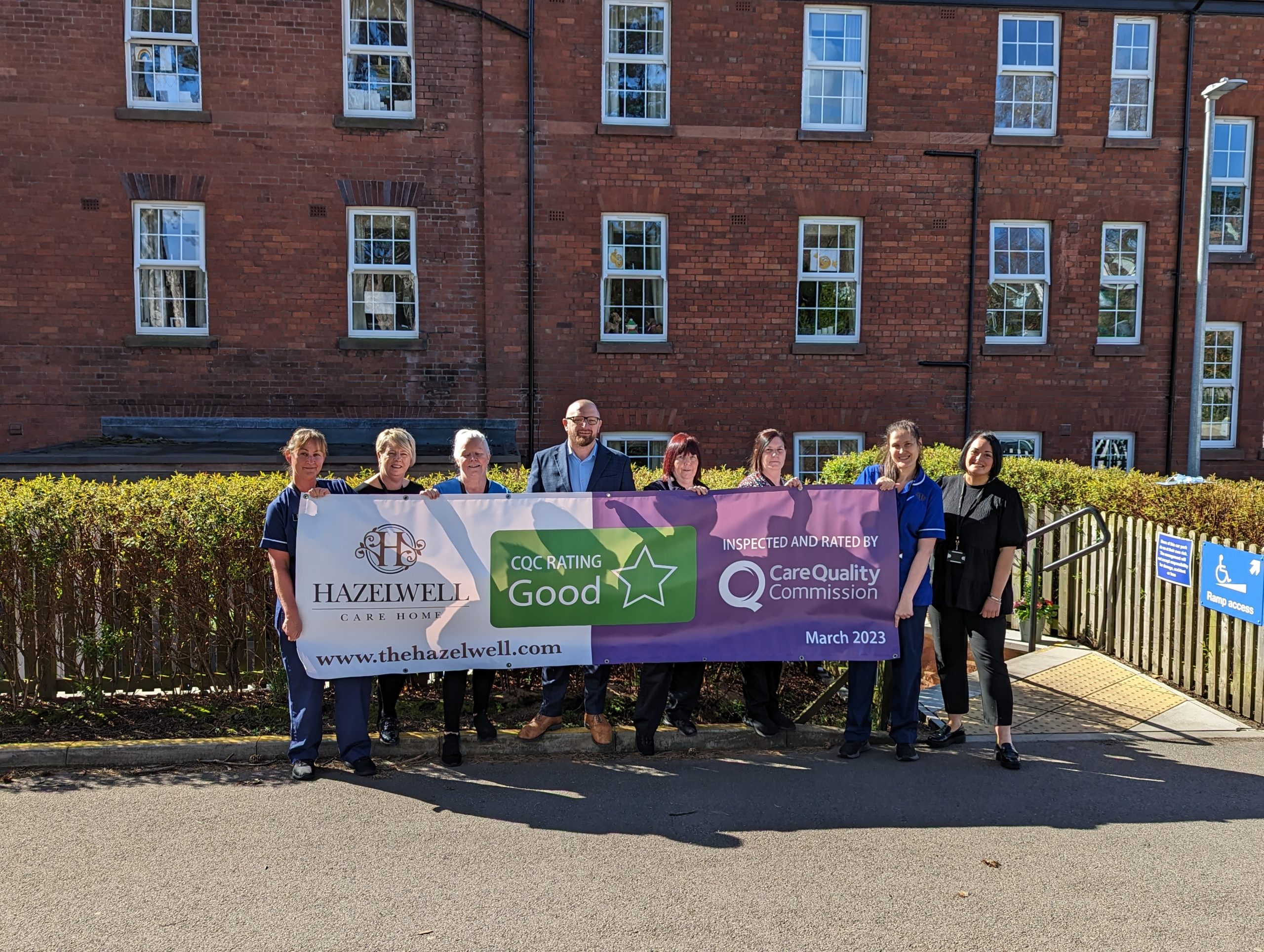 A team photo our care staff with a banner of our CQC rating at Hazelwell Care Home